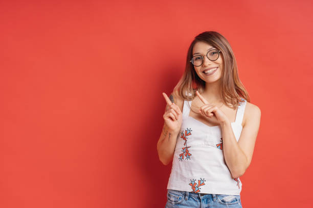 istock Smiling young female with glasses, pointing aside to red background 1161932387