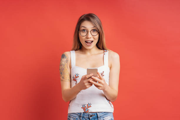 istock Surprised cute girl with a phone in hands on red background in studio 1161932388