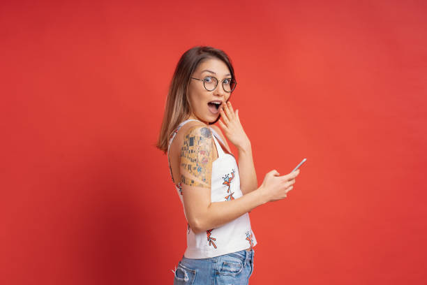 istock Surprised cute girl with a phone in hands on red background in studio 1161932393