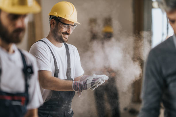 幸せな建設労働者は、改装アパートでおがくずから彼の手袋を掃除します。 - maintenance engineer home improvement men manual worker ストックフォトと画像