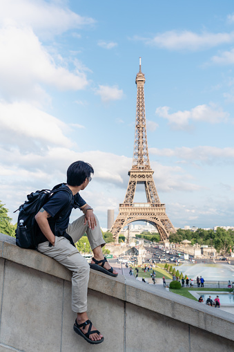 Traveling in Europe in summer, a man with backpack looking at Eiffel tower, famous landmark and travel destination in Paris, France