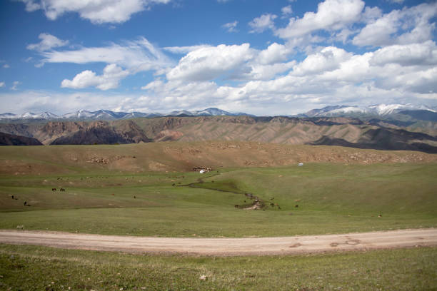 istock The road through the pasture between the hills with mountain ridges with snow covered peaks on the horizon. 1161944113