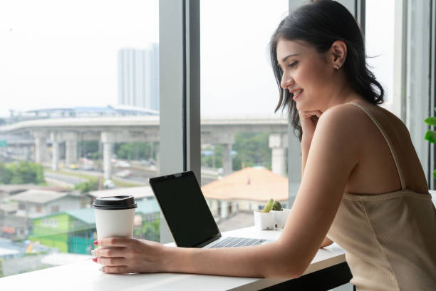 istock Young business woman using laptop computer while sitting at cafe table next to office windows. 1161944527