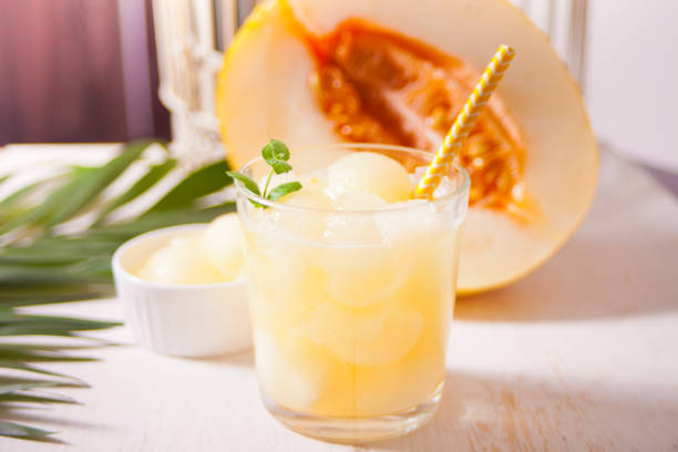 Glass with melon cocktail on a white table with the palm leaf in tropical theme stock photo