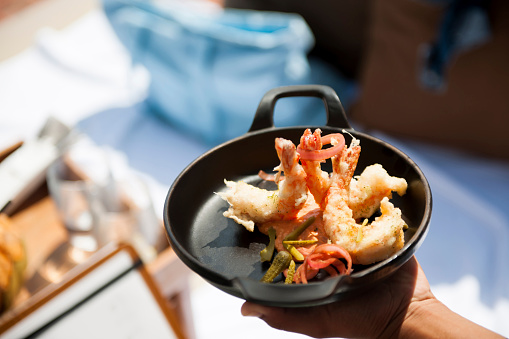 Close up photo of hands of waiter holding  fried shrimps food on the beach, people in the background out of focus