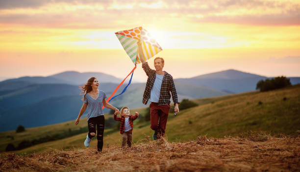 o pai feliz da família do filho da matriz e da criança lanç um papagaio na natureza no por do sol - grass summer day sunset - fotografias e filmes do acervo