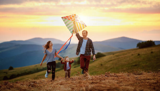 lycklig familj far till mor och barn son lansera en drake på naturen vid solnedgången - flying kite bildbanksfoton och bilder