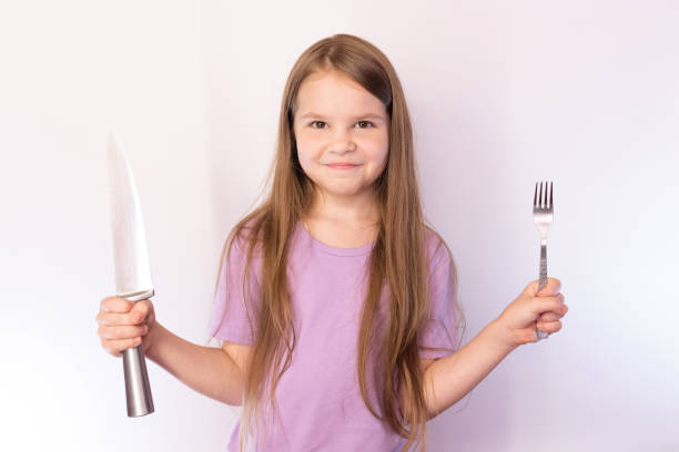 istock Little cute girl holding a knife and fork, with a satisfied expression on her face, on a light background 1161956134