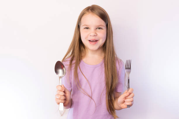 istock Little cute girl holding a spoon and fork with a satisfied expression on her face, on a light background 1161958542