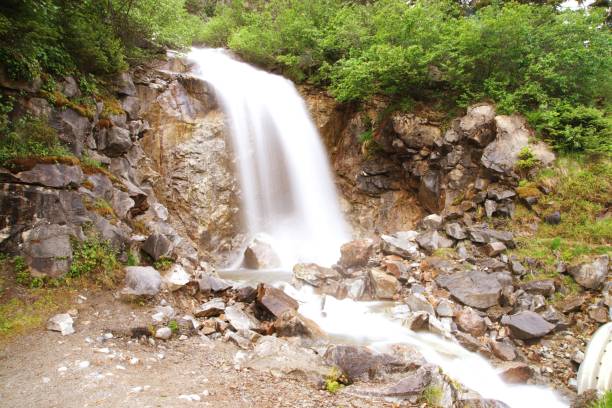 Side view of Waterfall in Alaska outside of Sagway, with pine trees, rocks, and gravel.