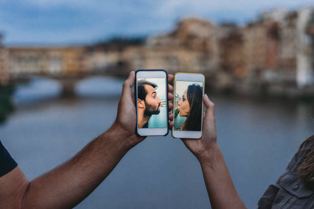 conceptual shot of a young adult couple kissing via mobile phone - internet dating imagens e fotografias de stock
