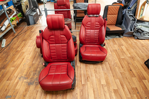 Four sport seats with red leather trim, located on the floor in the workshop for repair and tuning of cars and vehicles