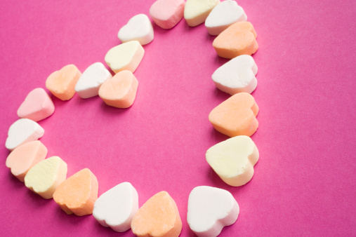 multicolored sugar candies arranged in a heart shape on a pink background