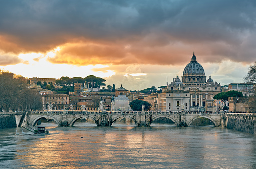 Rome, Italy - December 23,2022: St. Peter's Basilica in Rome, Italy, as the sun sets, casting a warm glow on the majestic structure, while the Tiber River gracefully reflects the colors of the Roman sky