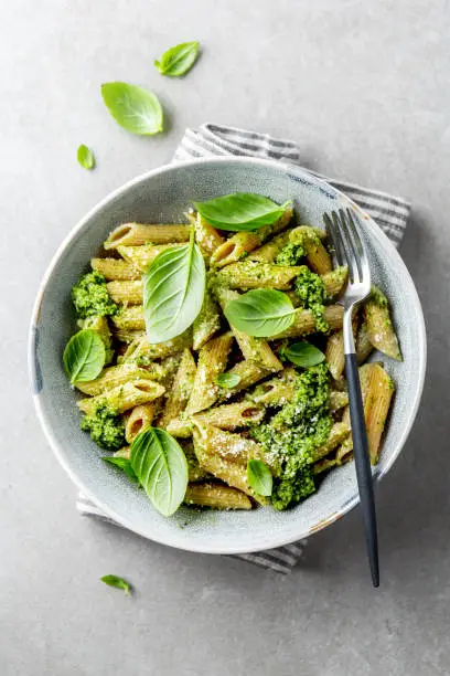 Tasty appetizing wholegrain pasta with pesto sauce, parmesan cheese and basil served on plate on grey background.