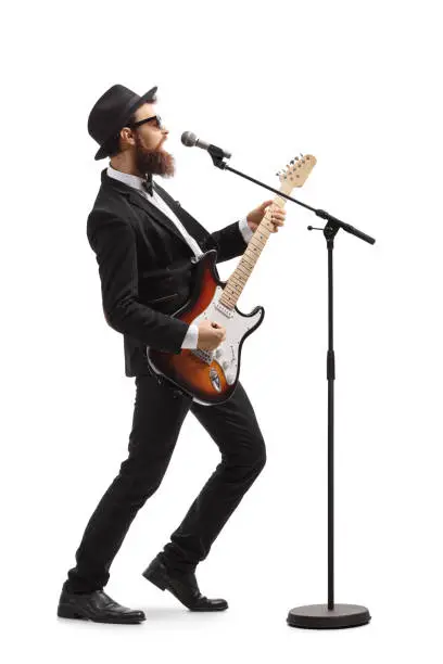 Full length profile shot of a male artist playing a bass guitar and singing on a mic isolated on white background