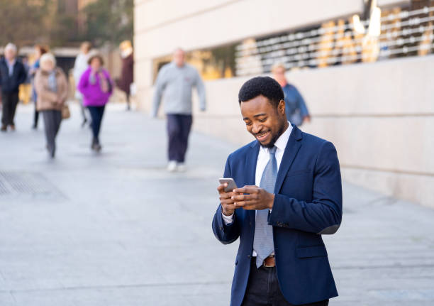 istock Young man in smart wear on mobile phone sending text email or social media app outdoors at city street. Happy business people, working outside, entrepreneur and work freedom communication technology. 1161988310