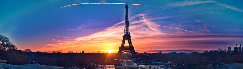 Wide shot of the iconic Eiffel Tower in Paris, France, with tourists and vehicles on a partly cloudy day.