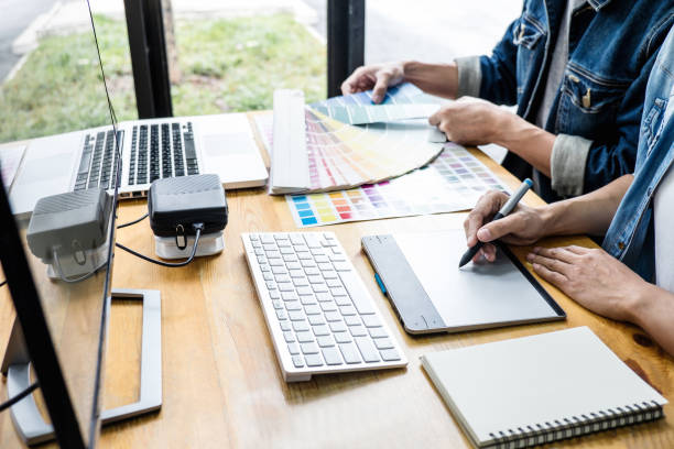 istock Two colleagues creative graphic designer working on color selection and drawing on graphics tablet at workplace, Color swatch samples chart for selection coloring 1161989345
