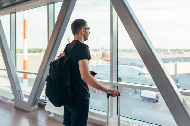 istock Young man standing near window at airport 1161989625