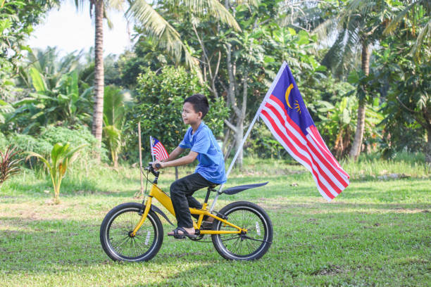 A Malay Muslim boy riding on a bicycle with Malaysian flags attached to it, to celebrate Malaysia's National Day.
