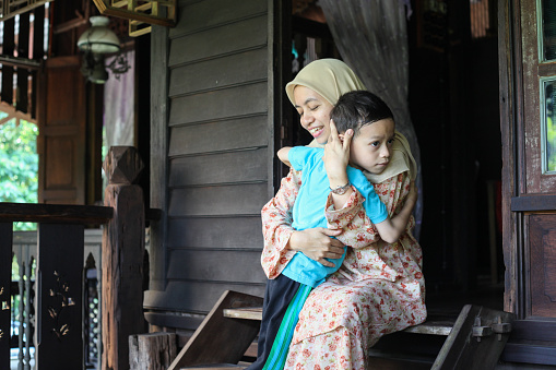 A Malay Muslim mother doing her best to comfort her son by hugging him.