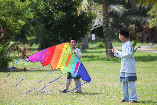 Two Malay Muslim boys in traditional Malay costume playing kite on a field.