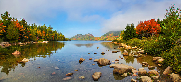 Panoramic view of the clear water, stones and fall foliage of Jordan Pond in Acadia National Park