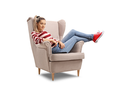 Young woman seated in an armchair watching TV isolated on white background