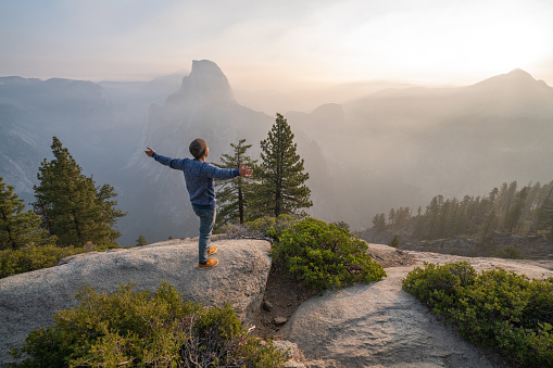 Young man cstamding arms outstretched on top of Yosemite valley, USA at sunrise