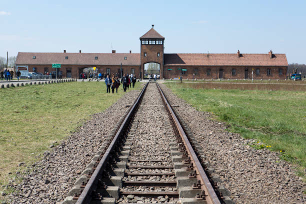 the Auschwitz-Birkenau concentration camp, located in Poland in Central Europe.  Railroad tracks lead to the main entrance building.  Visitors gather near the entrance.