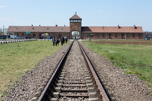the Auschwitz-Birkenau concentration camp, located in Poland in Central Europe.  Railroad tracks lead to the main entrance building.  Visitors gather near the entrance.