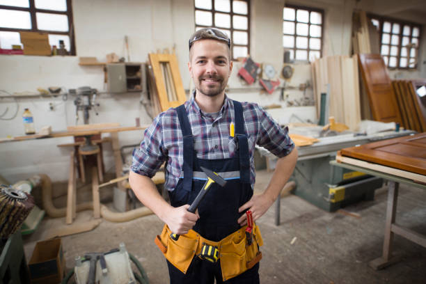 istock Portrait of smiling handsome craftsman holding hammer in his workshop. Skillful creative man in production factory. 1162003736