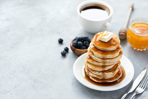 Pancakes with butter, syrup and cup of coffee on concrete backdrop. Copy space for text. Classic American breakfast