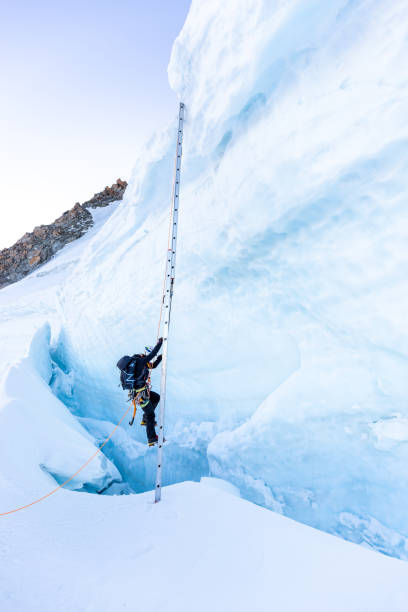 アルピニスト登山家は氷のクレバスの上にはしごを登る。 - crevasse ストックフォトと画像