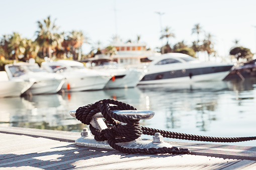 Mooring yacht rope with a knotted end tied around a cleat on a wooden pier against marina view