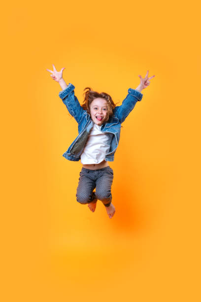 retrato de longitud completa de la niña rizada saltando sobre el fondo naranja - playing playful baby contemporary fotografías e imágenes de stock