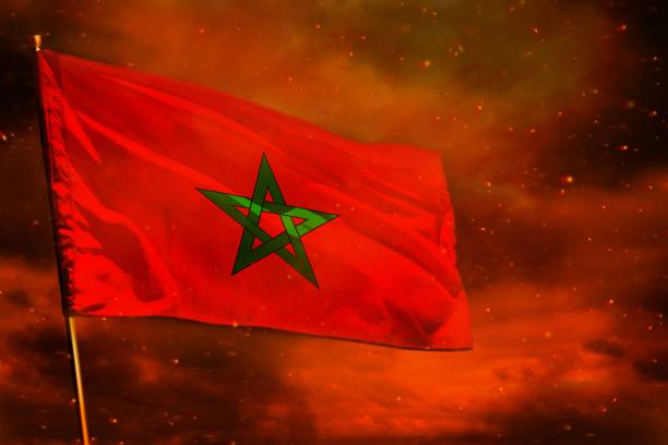 istock Fluttering Morocco flag on crimson red sky with smoke pillars background. Troubles concept. 1162034272