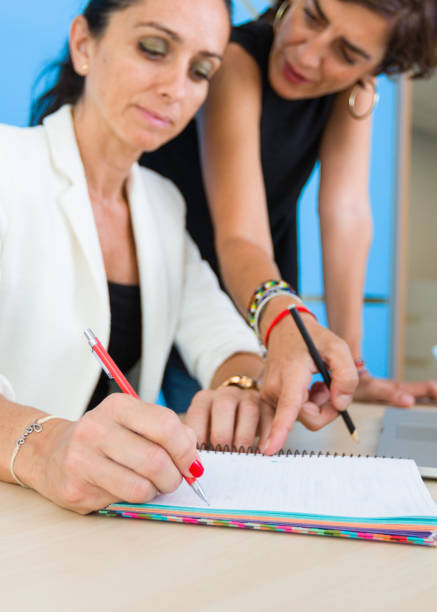 istock A woman standing points to another who is writing where she has to pay attention 1162041535