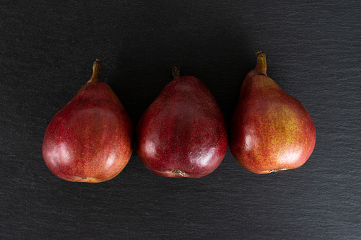 Group of three whole fresh dark red pear anjou flatlay on grey stone