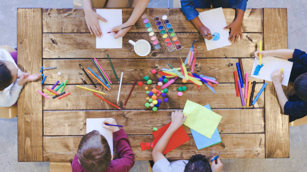 Aerial view of kids doing arts and crafts Aerial overhead view of a multi-ethnic group of elementary age children doing arts and crafts. The kids are seated around a large table that is covered by coloring and painting supplies. The creative kids are having fun and sharing. jib stock pictures, royalty-free photos & images