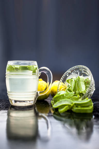 Close up of glass mug on wooden surface containing aloe vera and lemon juice detox drink along with its entire raw ingredients with it. Vertical shot with blurred background. stock photo