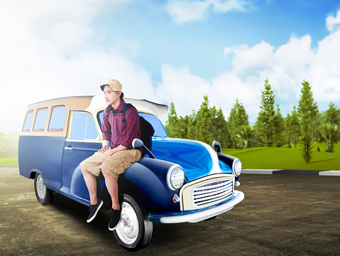 Asian man in hat with backpack sitting on the car hood at road with green trees and blue sky background. Traveling concept