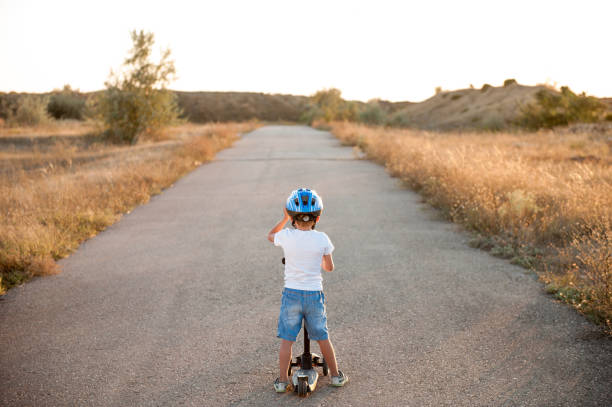istock active sport little boy in helmet standing on empty asphalt road with scooter on summer warm sunset 1162077657