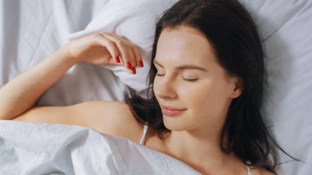 portrait de la belle jeune brunette qui se réveille avec charme dans son lit et qui sourit sensuellement, son visage est illuminé par le soleil chaud du matin. top down shot. - charmingly photos et images de collection