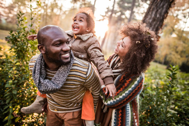 Happy black parents having fun with their daughter at the park. Happy African American family having fun in autumn day at the park. Father is piggybacking little girl. african father stock pictures, royalty-free photos & images