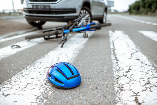 Scene of a road accident with car and broken bicycle lying on the pedestrian crossing. Helmet on the foreground