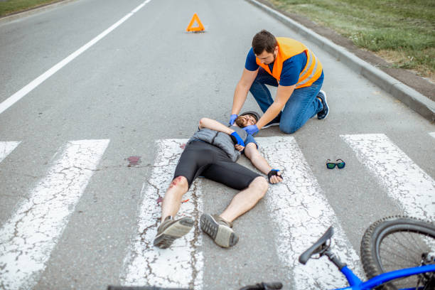 istock Road accident with injured cyclist and man providing first aid 1162083856