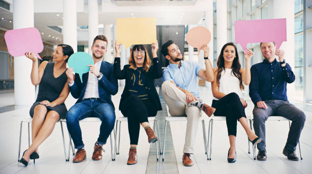 I'm the ideal candidate because... Shot of a group of businesspeople holding colorful speech bubbles while waiting in line in a modern office endorsing photos stock pictures, royalty-free photos & images
