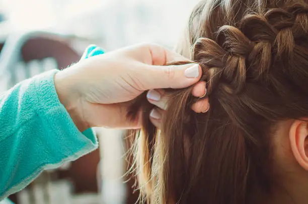 The hairdresser plaits the braid girl. Hands, close-up. Pretty haircut.